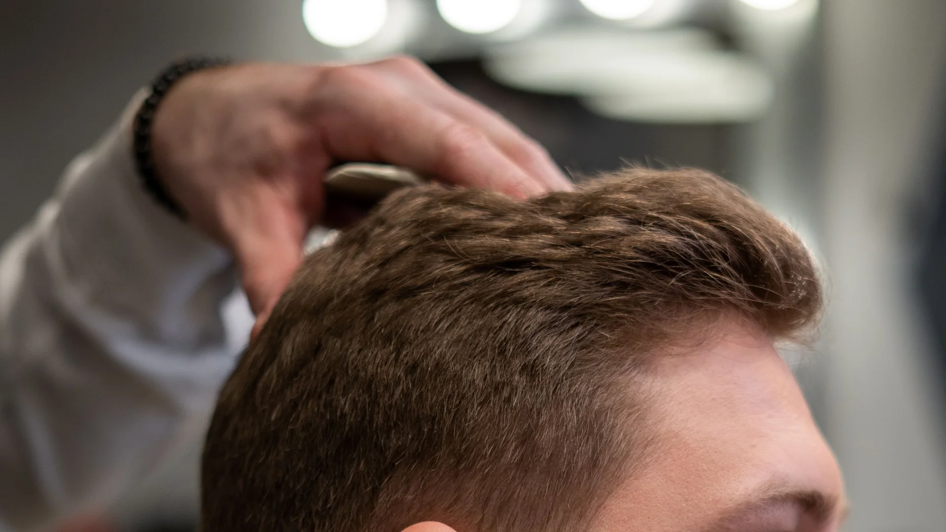 Barber shaping a client’s hair with shears in warm atelier light